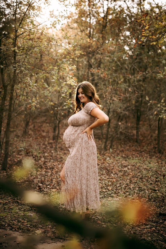 Maternity Photographer, a woman holds her pregnant belly as she stands in the forest