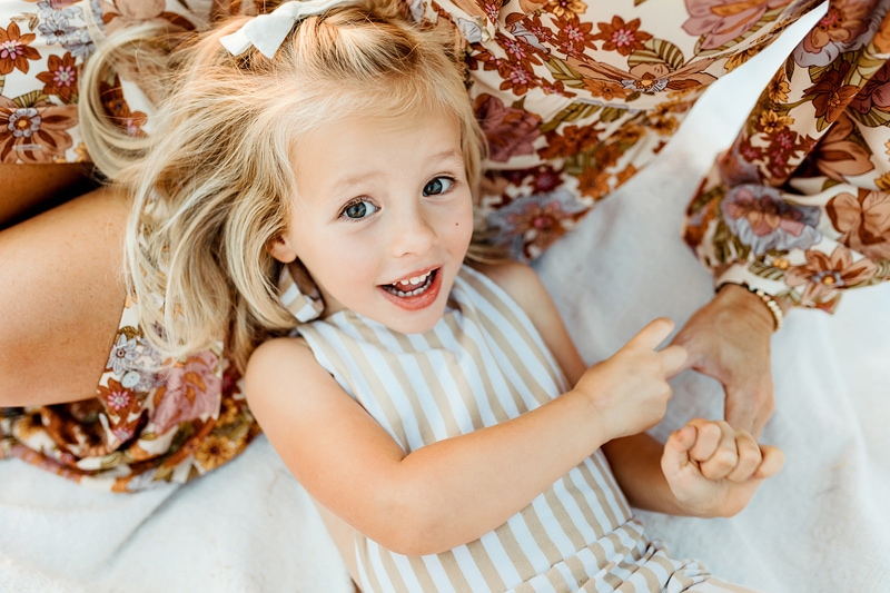Family Photographer, a young girl laughs with a big bright smiles as she lays on mom's lap