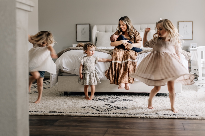mom holding newborn and sisters twirling at home