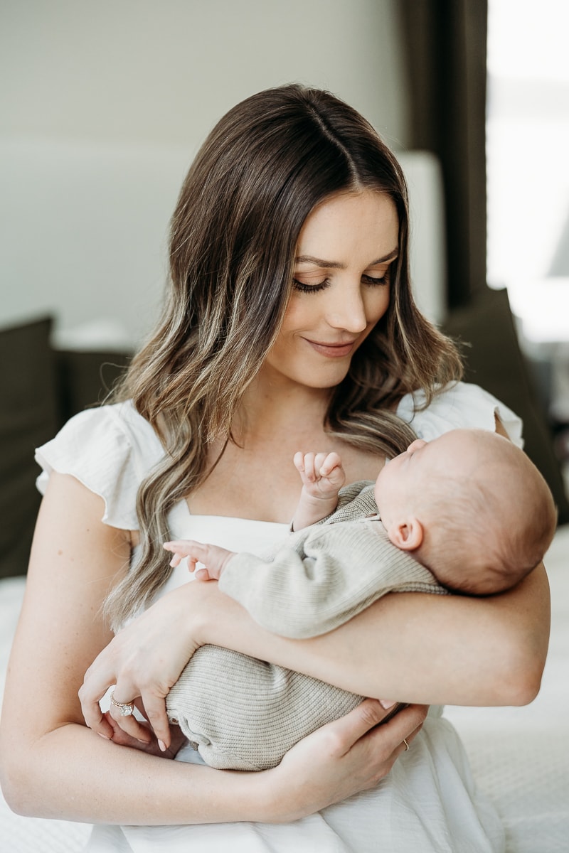 mom with white dress holding newborn baby in neutral outfit